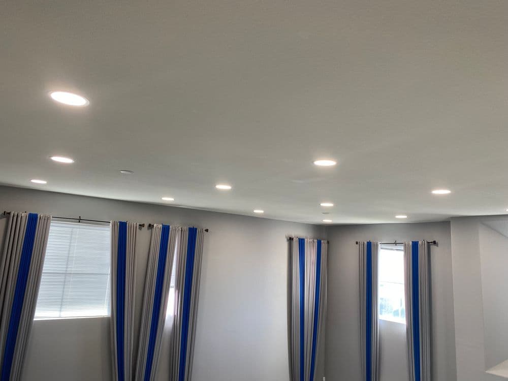 Modern living room with recessed lighting and striped curtains by windows.