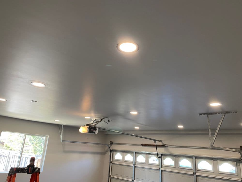Brightly lit garage ceiling with recessed lights and garage door opener, showcasing a modern design.