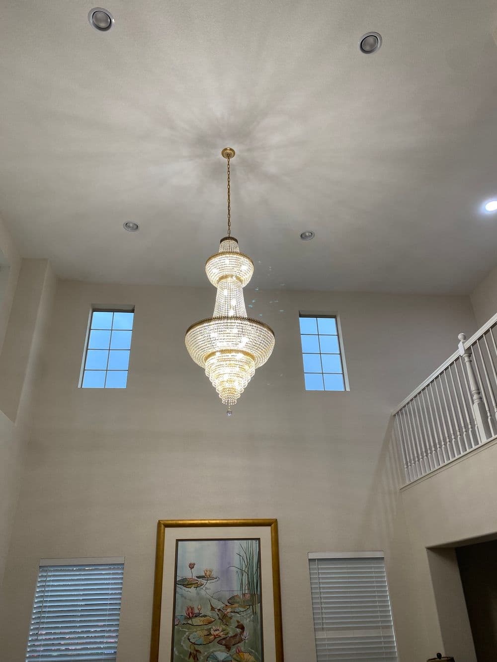 Elegant crystal chandelier hanging in a spacious foyer with large windows and artwork.