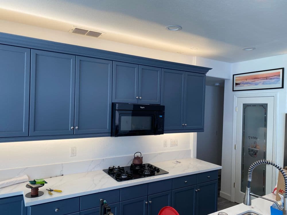 Modern kitchen with blue cabinetry, white countertops, black microwave, and gas stove.