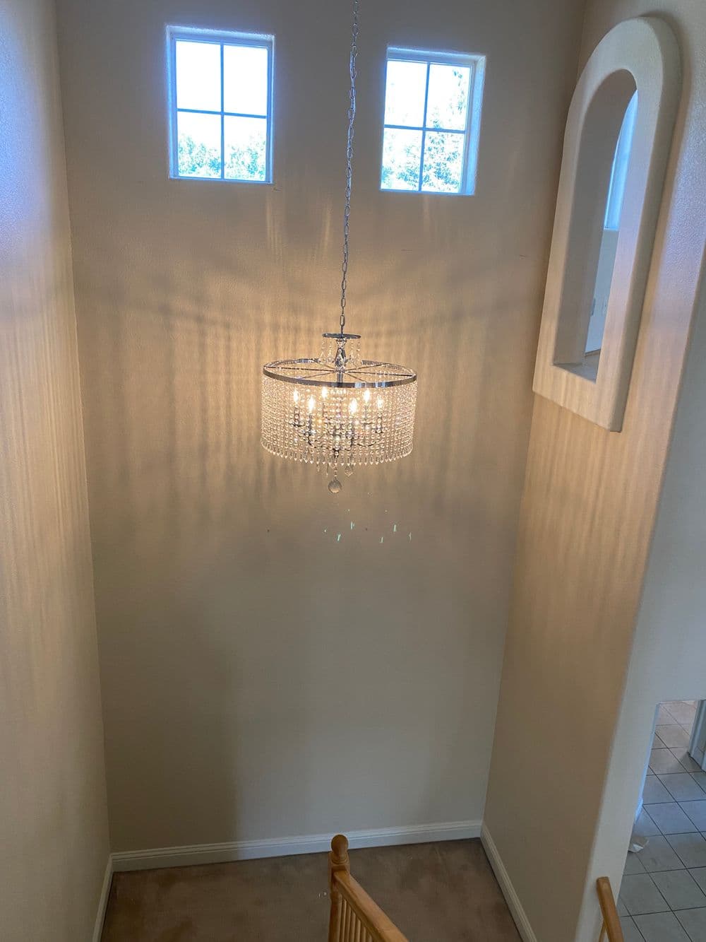 Elegant crystal chandelier hanging in a brightly lit stairwell with two windows.
