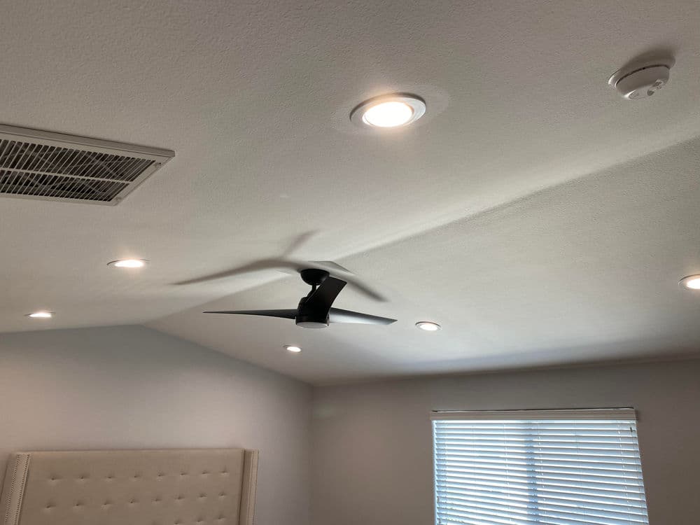 Ceiling with modern ceiling fan, recessed lights, and smoke detector in a bright room.