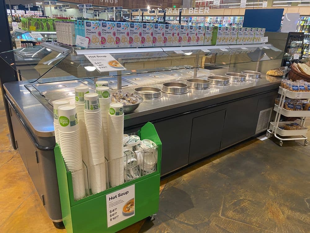 Soup station with multiple containers and pricing information in a grocery store.