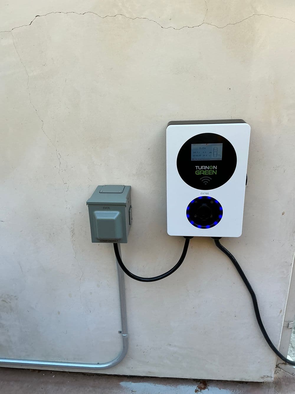 Electric vehicle charger mounted on a wall with monitoring screen and power connection.