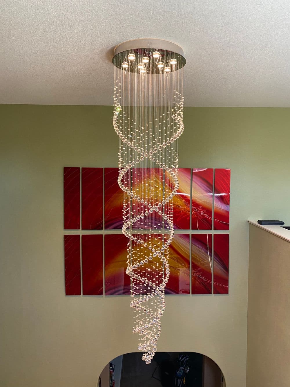 Modern chandelier featuring a spiral design made of crystals, hanging above colorful wall art.