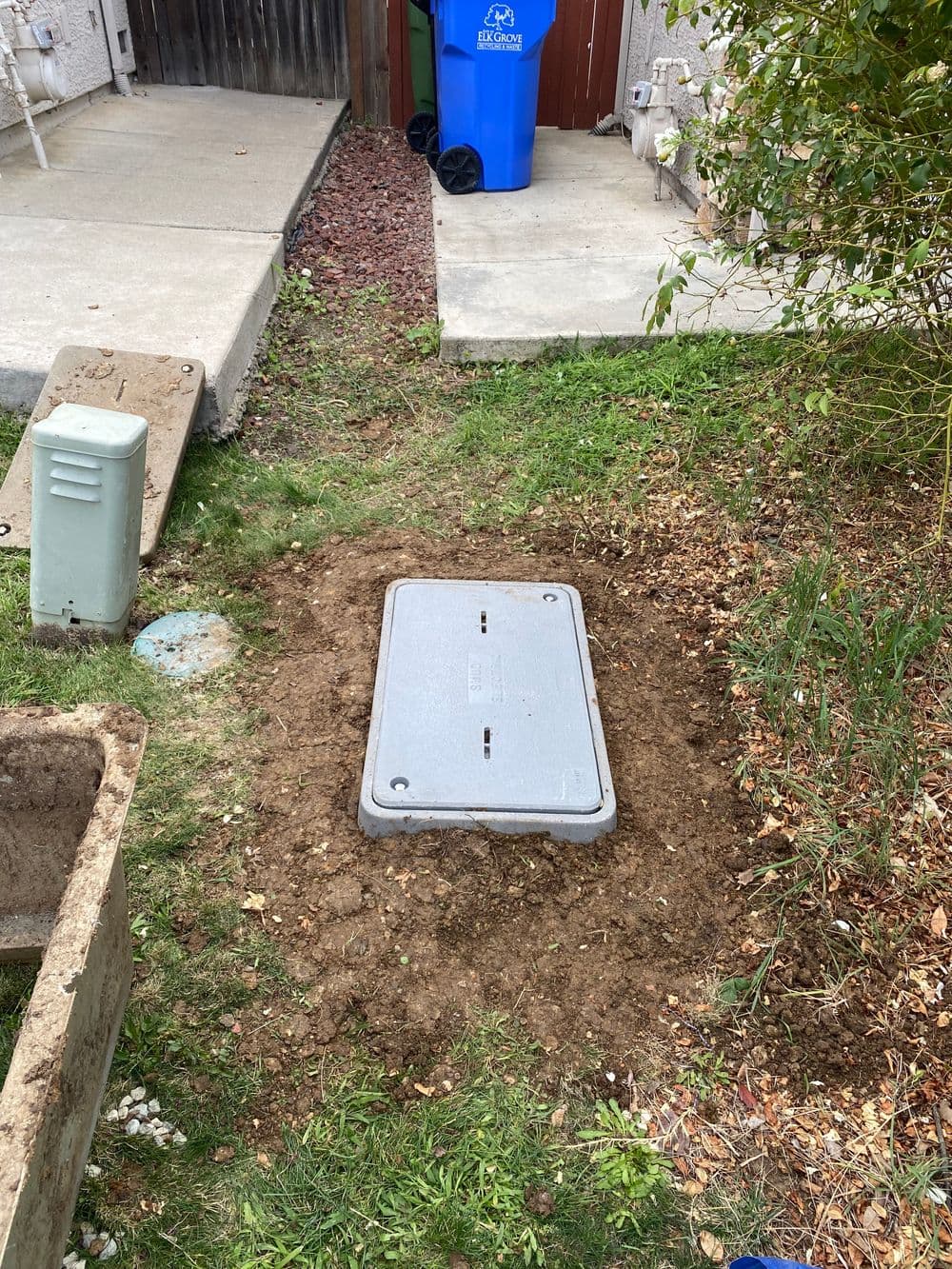 Utility access point cover situated in a grassy yard with nearby utility boxes.