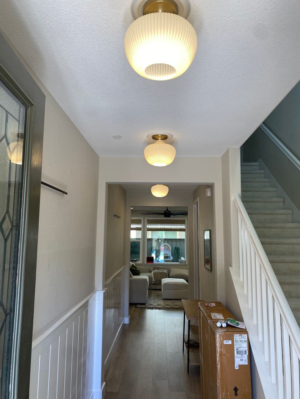 Bright hallway with modern light fixtures, leading to a cozy living room and staircase.