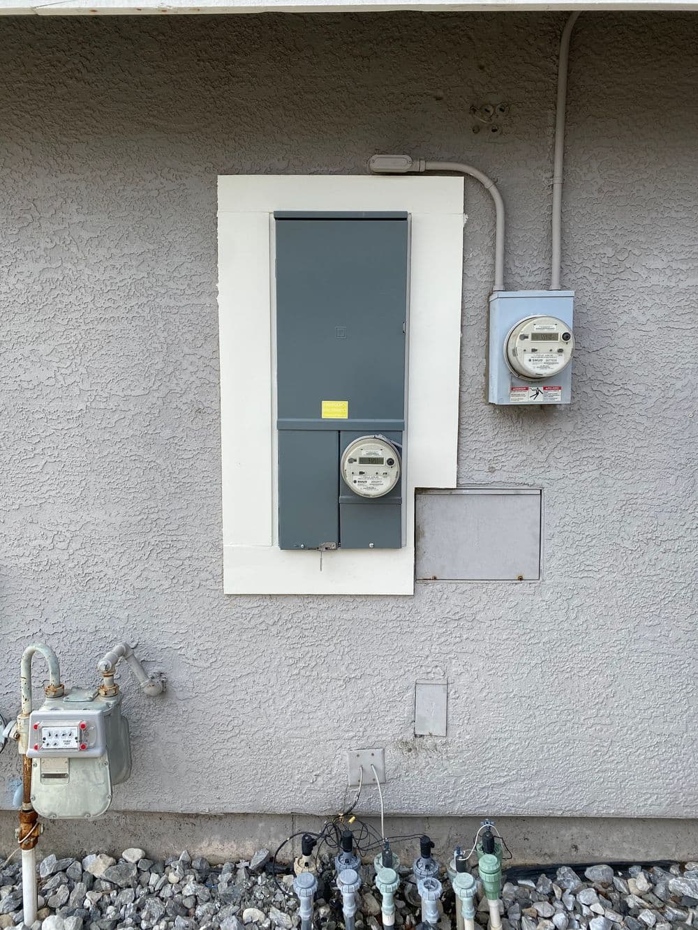 Electrical meter and panel mounted on a gray wall with gas meter below.