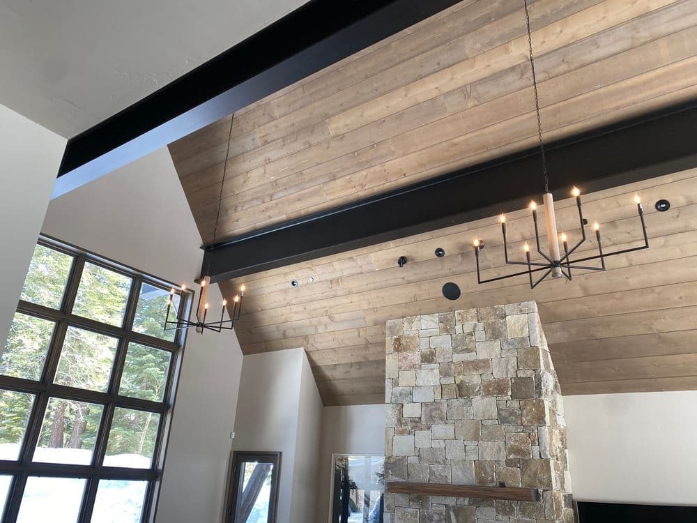 Modern interior with high wooden ceiling, stone fireplace, and stylish hanging chandeliers.