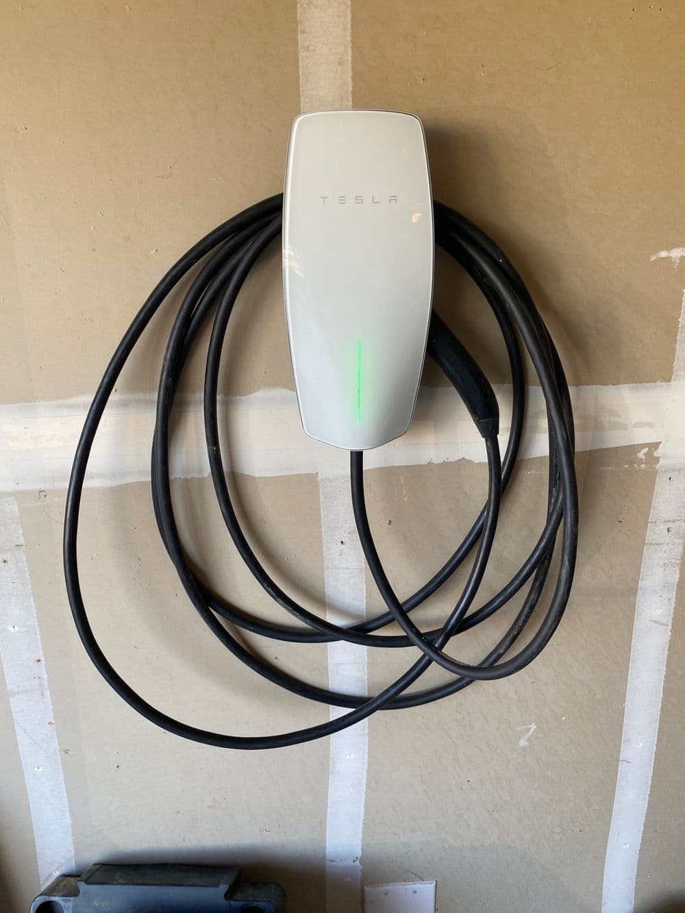 Tesla wall-mounted electric vehicle charger with coiled cable, green indicator light.