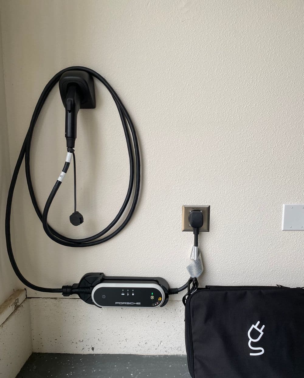 Porsche electric vehicle charger mounted on a wall with charging cable and bag.