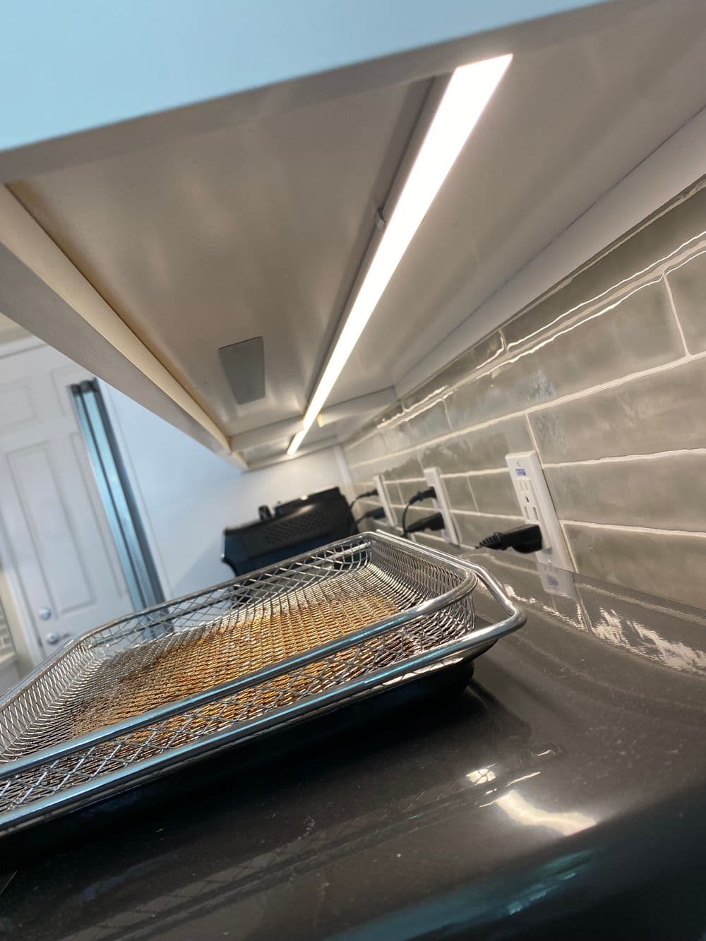 Modern kitchen with sleek backsplash, overhead lighting, and wire cooling rack on countertop.