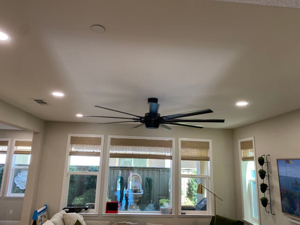 Modern ceiling fan in bright living room with large windows and natural light.