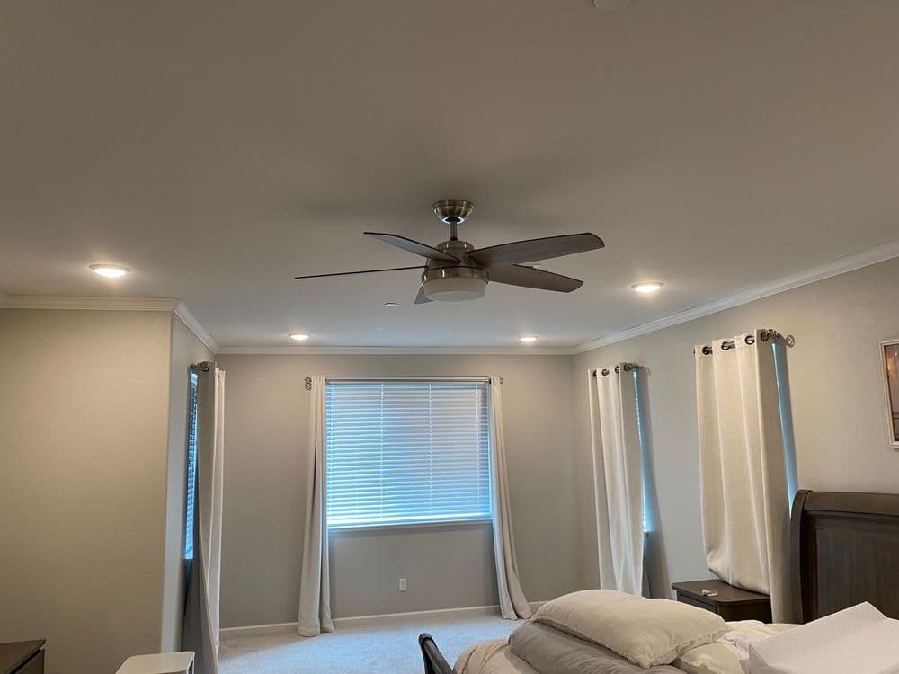 Cozy bedroom with ceiling fan, large window, and light-colored curtains. Modern design.